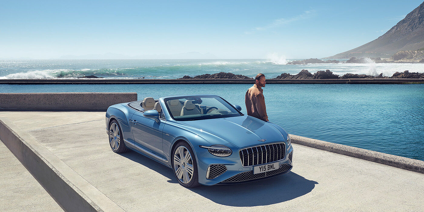 Bentley Bangkok New Bentley Continental GTC Azure convertible front view in Light Windsor blue paint with 22 inch ten spoke wheels parked by the sea in the sunshine