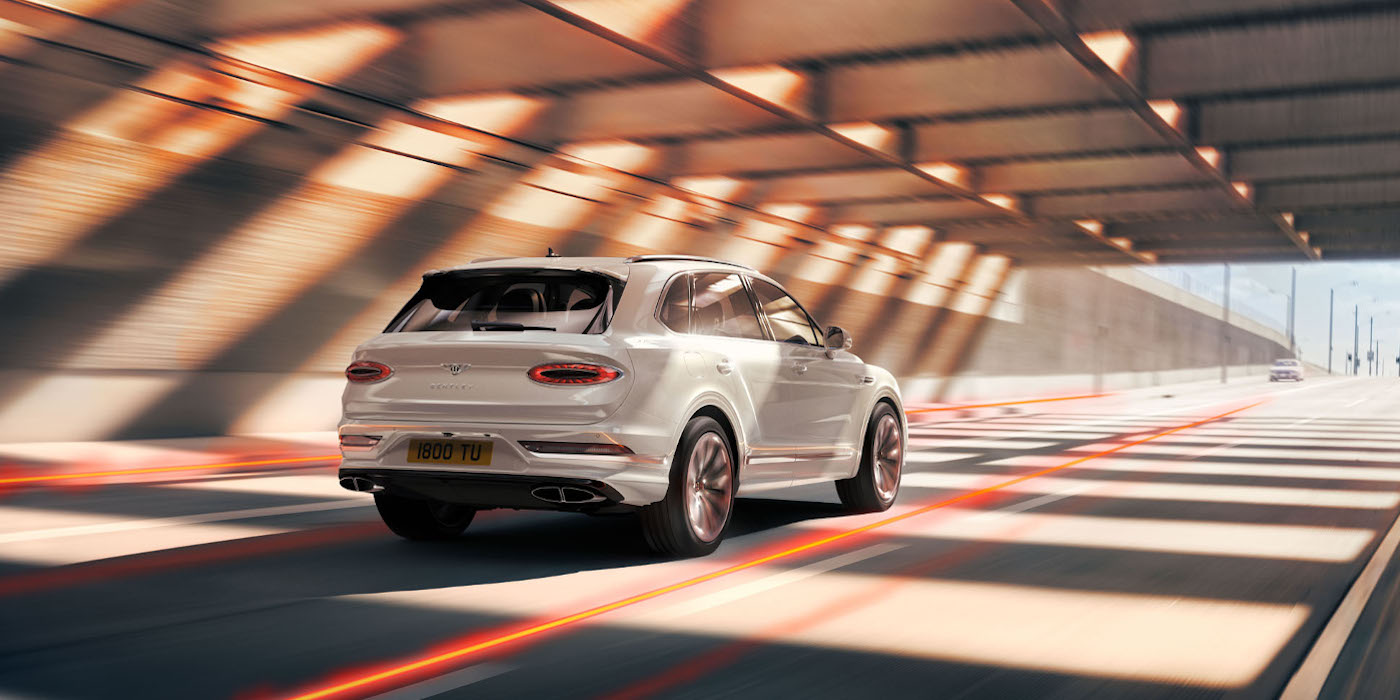 new-bentley-bentayga-hybrid-in-ice-white-paint-rear-three-quarter-driving-in-tunnel-los-angeles