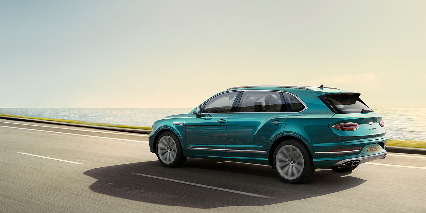 Bentley Bangkok Rear view of a Topaz blue Bentley Bentayga EWB Azure, cruising along a sea side road.