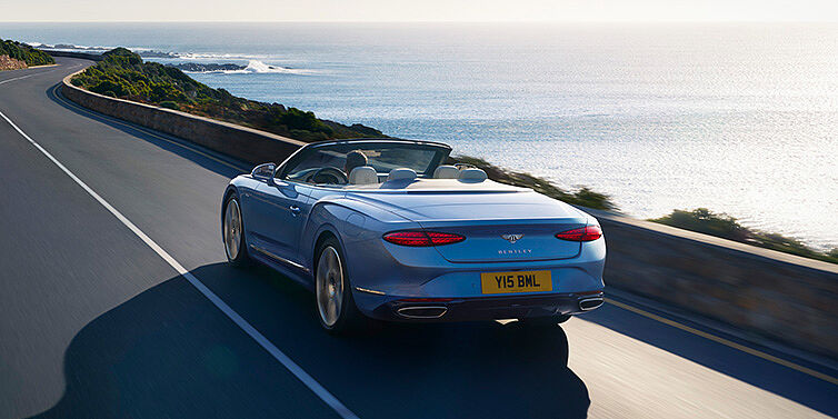 Bentley Bangkok New Bentley Continental GTC Azure convertible rear view in Light Windsor blue paint with 22 inch ten spoke wheels driving dynamically on an ocean road in the sunshine