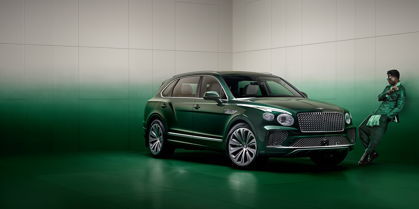 Bentley Bangkok Wisdom K leans against wall next to Bentley Bentayga Extended Wheelbase Atelier Edition SUV in Light Emerald green paint