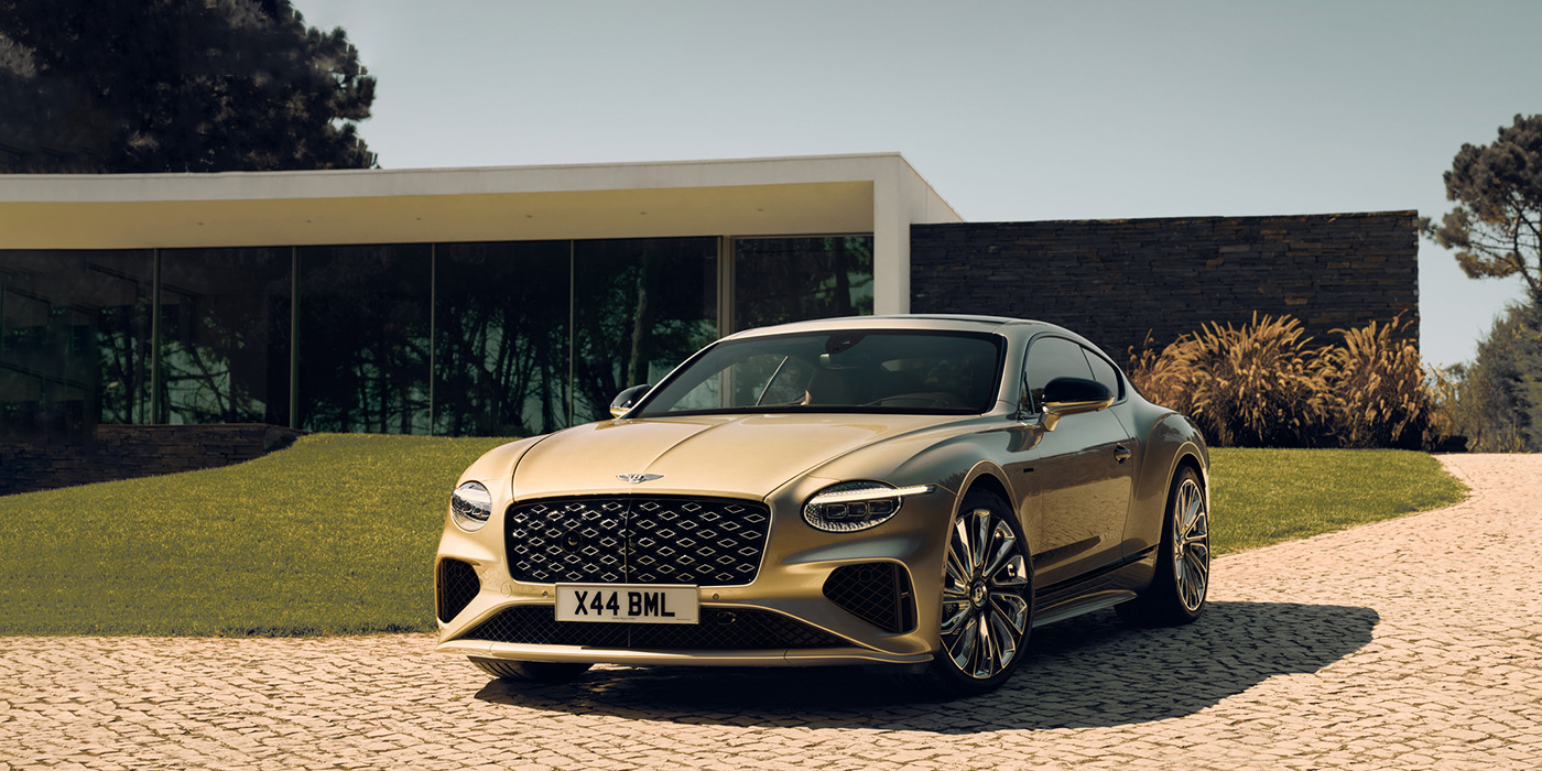 Bentley Bangkok Bentley Continental GT Mulliner coupe front three quarters in Patina paint parked outside a glass fronted building with a grass lawn behind it