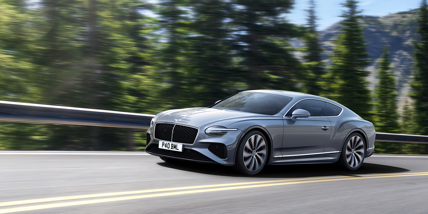 Bentley Bangkok New Bentley Continental GT coupe in Silverlake paint and 22 inch ten-spoke wheels, driving dynamically on a tree-lined road in the sunshine