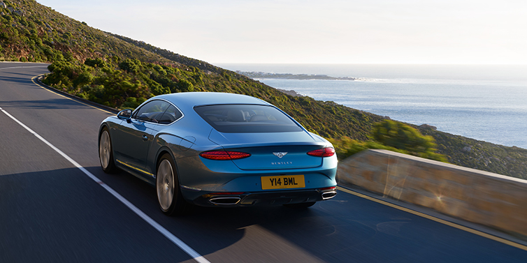 Bentley Bangkok New Bentley Continental GT Azure coupe in Light Windsor blue paint seen from the rear driving dynamically on a seaside road